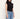 A woman wearing a black sleeveless mock neck top and light blue jeans, shown from the chest down against a plain off-white background.