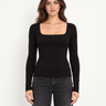 A woman wearing a black square neck long sleeve top and black jeans on a white background 