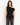 Delilah black drape top, front view showing asymmetrical off-the-shoulder neckline with dark jeans