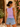 Woman wearing a purple tank top and denim shorts standing in a garden.