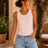 Woman wearing a light pink tank top and denim shorts standing in a sunlit outdoor setting.
