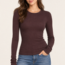 A woman modeling a fitted, long-sleeve crewneck top in dark brown, paired with blue jeans, against a plain off-white studio background.