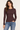 A woman modeling a fitted, long-sleeve crewneck top in dark brown, paired with blue jeans, against a plain off-white studio background.