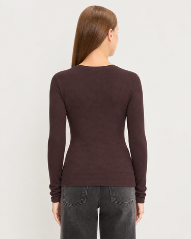 A woman viewed from the back wearing a fitted long-sleeve crew-neck top in dark brown, paired with dark gray jeans, against a light gray studio background.