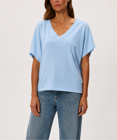 Woman wearing a light blue top and jeans on a plain background