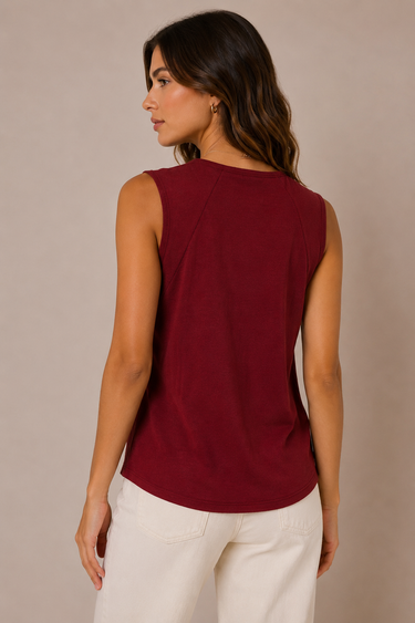 A woman shown from the back wearing a sleeveless, boat-neck top in deep burgundy and white pants, set against a plain beige studio background.