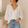 Woman wearing a white blouse and blue jeans against a neutral background