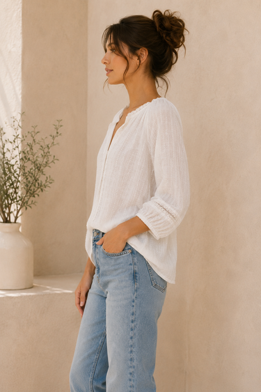 Woman wearing a white blouse and light blue jeans against a beige wall.