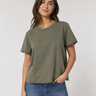 A woman wearing a relaxed-fit, short-sleeve crewneck t-shirt in olive green, paired with blue jeans, standing against a light gray studio background.