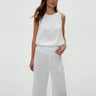 Woman wearing a white sleeveless top and pants on a plain background