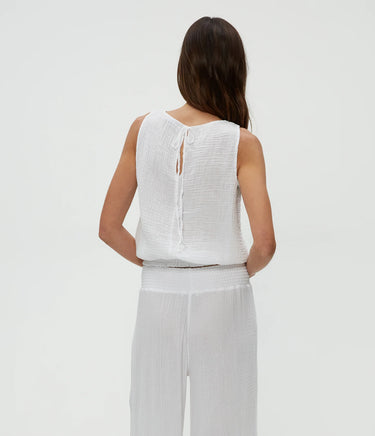 Woman wearing a white sleeveless top and pants on a light gray background