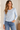 A woman wearing a light blue  long sleeve crew tee and blue jeans on a white background.