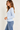 A woman wearing a light blue long sleeve crew tee and blue jeans on a white background.