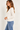 A woman wearing a chalk long sleeve crew tee and blue jeans on a white background.