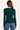 A woman viewed from the back wearing a fitted long-sleeve dark green top and blue jeans against a plain light background.