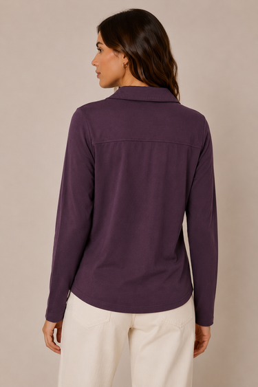 A woman shown from the back wearing a long-sleeve collared purple top and cream-colored pants, photographed against a plain beige studio background.