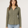 A woman modeling a long-sleeve button-up shirt in olive green, paired with light-wash blue jeans, against a plain light gray studio background.