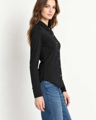 A woman wearing a black long-sleeve button-up shirt and blue jeans, shown from a side profile against a plain light background.