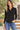 A woman wearing a black long-sleeve button-up shirt and blue jeans shown in an outside setting