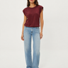 A woman modeling a sleeveless maroon top and light-wash blue jeans against a plain light gray studio background.