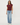 A woman modeling a sleeveless maroon top and light-wash blue jeans against a plain light gray studio background.