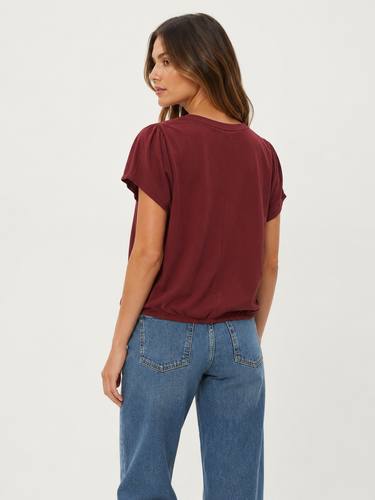 A woman shown from the back wearing a short-sleeve maroon t-shirt and blue jeans, photographed against a plain light gray studio background.