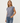 A woman modeling a muted slate blue-gray sleeveless crop top with a relaxed fit, paired with blue jeans, against a plain light gray studio background.