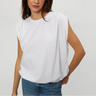 A woman wearing a white sleeveless top with a relaxed, draped fit and blue jeans, standing against a light gray studio background.