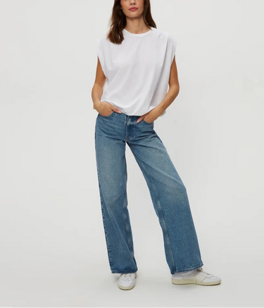 A woman wearing a cap sleeve white top and blue jeans on a white background