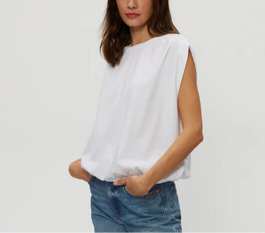 Woman wearing a white sleeveless top and blue jeans on a plain background