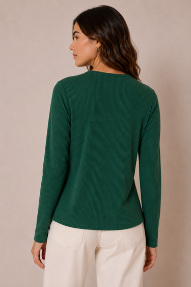 A woman shown from the back wearing a dark green ribbed long-sleeve top and cream-colored pants, standing against a solid beige studio background.