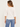 A woman shown from the back wearing a white three-quarter sleeve top and blue jeans against a plain off-white studio background.