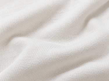 A close-up of soft, off-white knit fabric with a fine ribbed texture and gentle folds.
