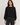 A woman modeling a black long-sleeve boat-neck top with balloon sleeves, paired with dark gray jeans, against a plain light gray studio background.