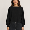 A woman modeling a black long-sleeve boat-neck top with balloon sleeves, paired with dark gray jeans, against a plain light gray studio background.