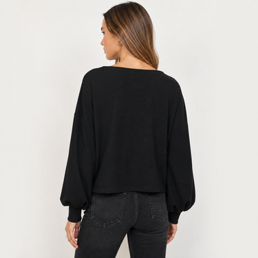 A woman shown from the back wearing a black long-sleeve top with balloon sleeves and dark gray jeans, photographed against a plain light gray studio background.