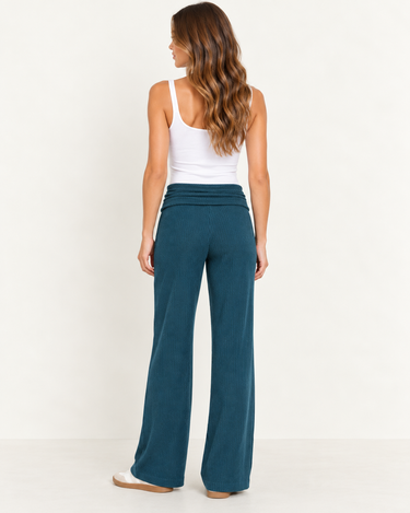 A woman wearing teal ribbed foldover pants, a white tank and sneakers on a white background.
