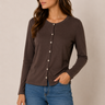 A woman wearing a dark brown long-sleeve button-front top and blue jeans, standing against a plain beige studio background.