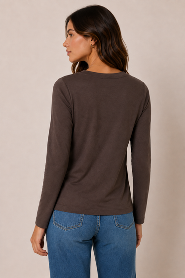 A woman shown from the back wearing a dark brown long-sleeve crewneck top and blue jeans, standing against a plain beige studio background.