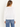 A woman facing backward wearing a white long sleeve and blue jeans on a white background.