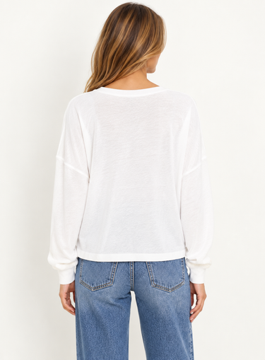 A woman facing backward wearing a white long sleeve and blue jeans on a white background.