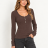 A woman wearing a scoop neck ribbed henley long sleeve tee in brown with black jeans on a white background.
