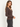A woman standing sideways wearing a scoop neck ribbed henley long sleeve tee in brown with black jeans on a white background.