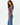 A woman modeling a long-sleeve crewneck knit top in a dusty mauve-purple color, paired with blue jeans, against a clean white studio background.