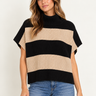 A woman wearing a beige and black stripe turtleneck poncho vest and blue jeans on a white background.