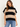 A woman wearing a beige and black stripe turtleneck poncho vest and blue jeans on a white background.