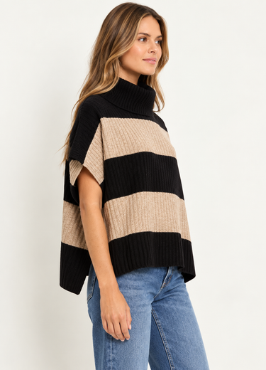 A woman wearing a beige and black stripe turtleneck poncho vest and blue jeans on a white background.