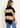A woman wearing a beige and black stripe turtleneck poncho vest and blue jeans on a white background.