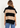 A woman wearing a beige and black stripe turtleneck poncho vest and blue jeans on a white background.