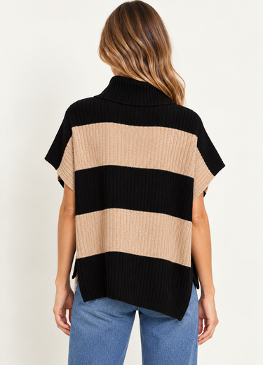 A woman wearing a beige and black stripe turtleneck poncho vest and blue jeans on a white background.